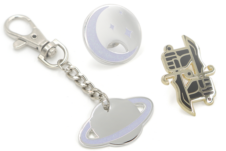 A collage of the dual wield studio logo pin, moon and stars charm pin, and glitter planet charm keychain