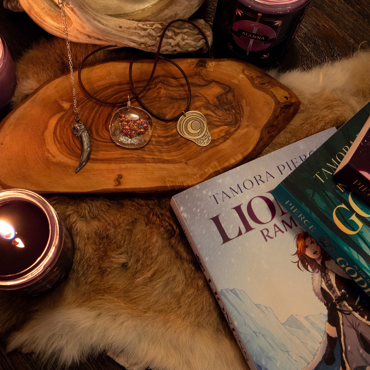 The silver badgerclaw necklace, the ember glass necklace, and the pregnancy charm laying beside one another on a slice of wood in a warm, cozy cabin.