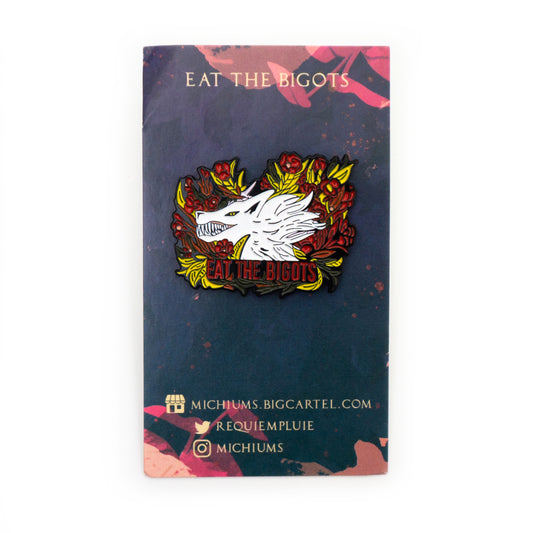 The Eat the Bigots pin on its backing card, which is navy with pink petals. “EAT THE BIGOTS” is emblazoned on the top, and the bottom has the artists’ contact information which is as follows: michiums.bigcartel.com, requiempluie on twitter, michiums on instagram