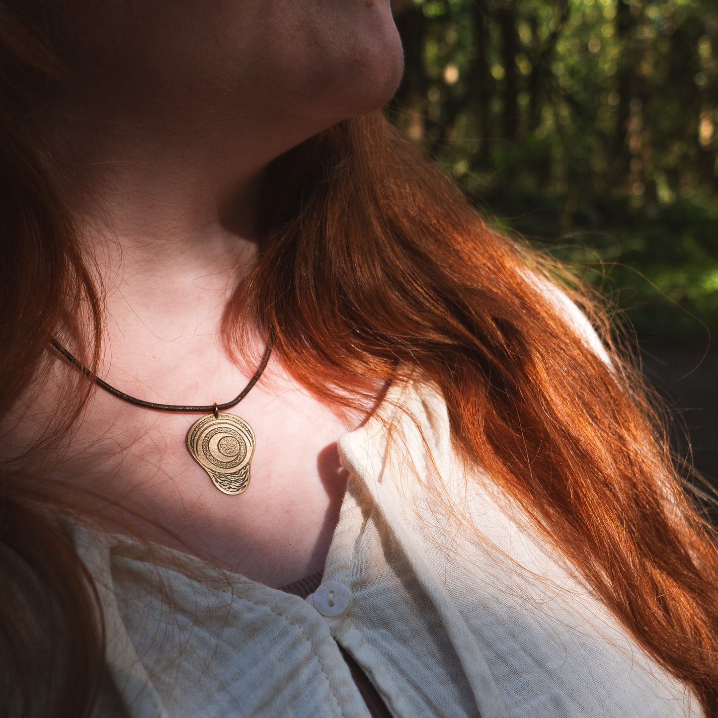 A closeup photo of the necklace being worn by a model in the forest. The necklace is catching the sunlight.