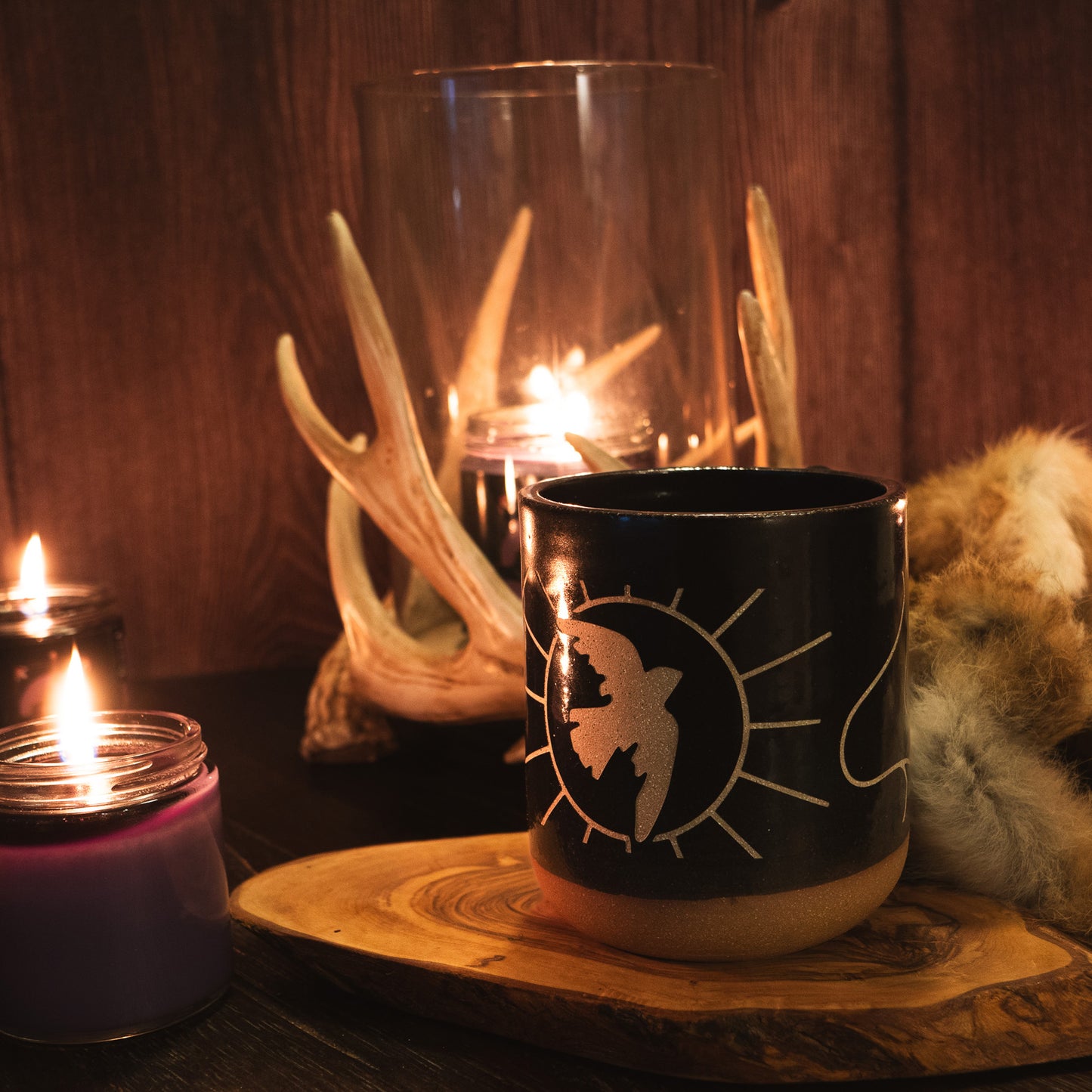 A photo of the dancing dove mug resting on a slice of wood, sorrounded by lit candles in a warm cabin.
