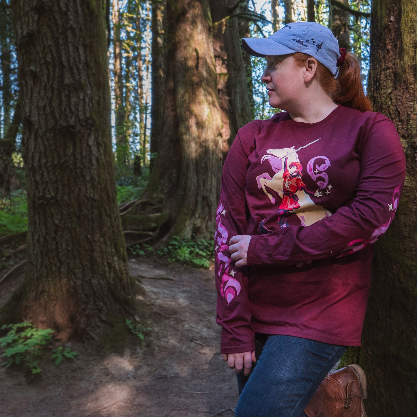 a model wears the maroon t-shirt and lavender ballcap in the woods.