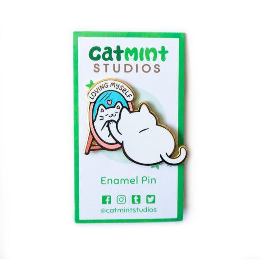 The Loving Myself Pin on its white backing card. “Catmint Studios” is across the top in green. Below the pin, it says “Enamel Pin” and “@catmintstudios” with the icons representing facebook, instagram, tumblr, and twitter.