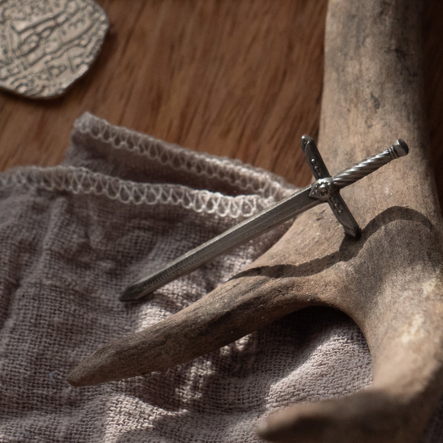 The lightning sword pin laying against a deer antler, the tip of the sword resting on a grey linen cloth.