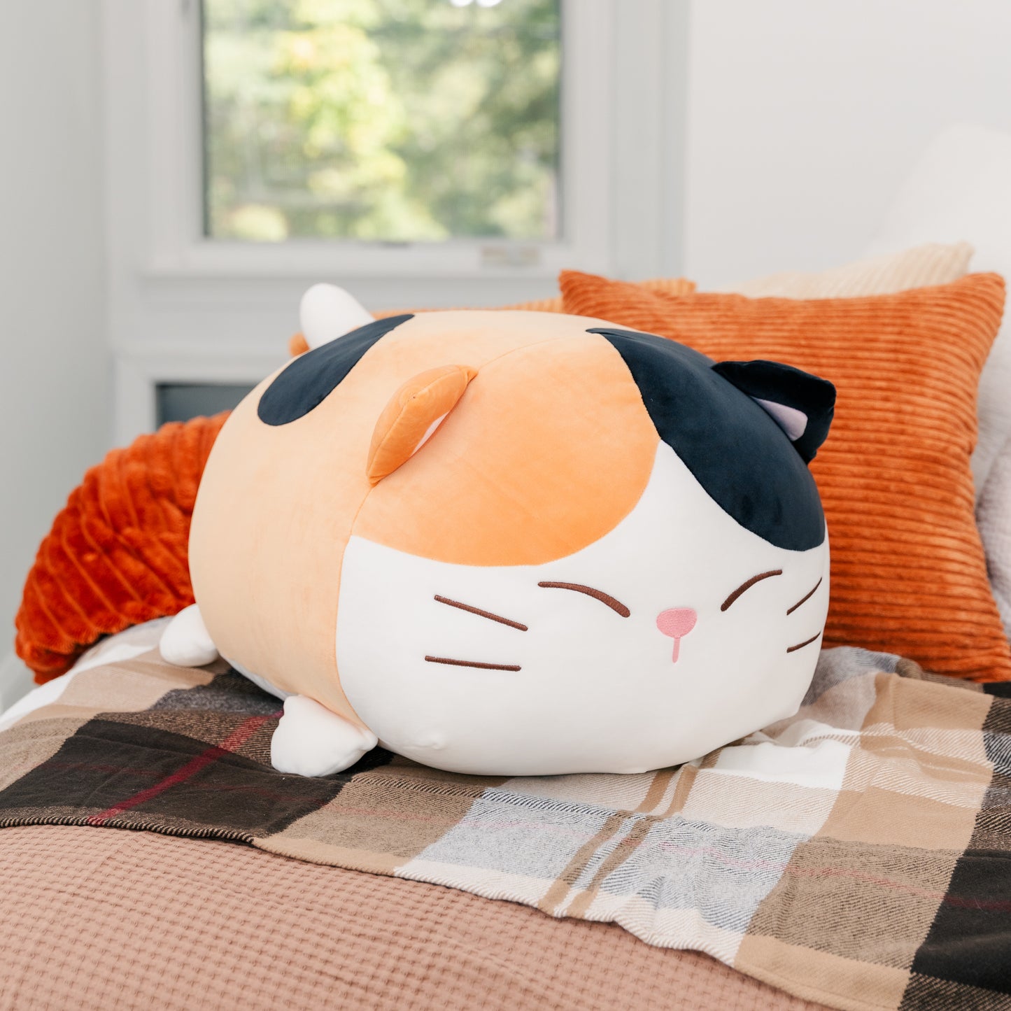 Plush Camang sitting on a blanket amongst pillows.