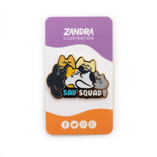 A product photo of the Sad Squad pin on its purple, white, and orange wavy colorblocked backing card. The backing card says Zandra Illustration at the top in white, and displays icons that signify the artist is on facebook, twitter, instagram, and etsy along the bottom of the card.