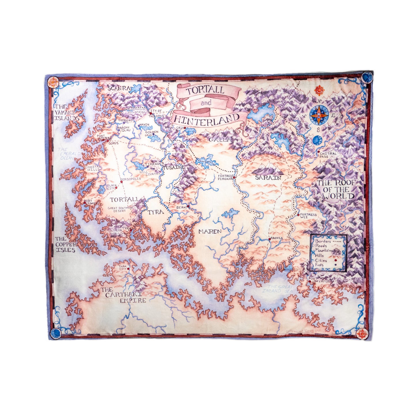 A flat lay photograph of the Tortall Map Sherpa-lined Blanket Violet Variant. A scroll at the top of the map reads “Tortall and Hinterland.” The entire map blanket is cool tones with pale violet mountains, a pale blue-purple sea. The land is slightly warmer tan with darker hues around hills and coasts. A blue and orange compass rose is toward the top right corner of the map, with a map key toward the bottom right. The map spans the mainland of Tortall and also includes The Copper Isles, the Yamani Islands,