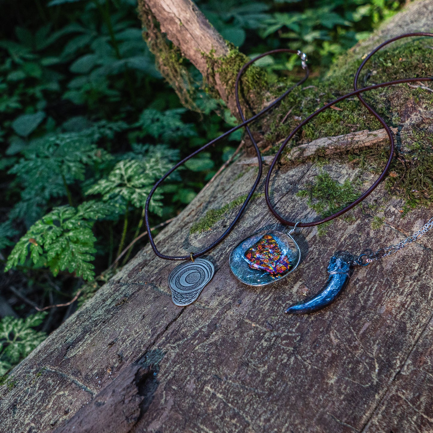 three necklaces - the badger claw, the ember glass, and the pregnancy charm - are draped over and resting on a mossy log.