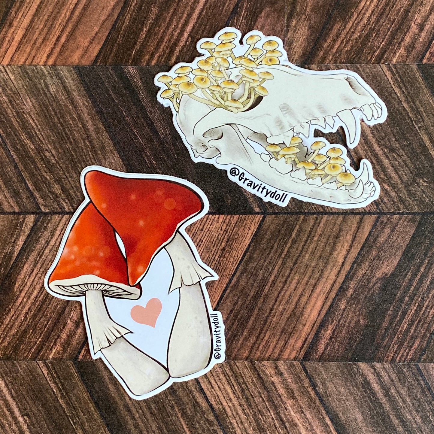 The honey fungus skull sticker on a wooden table next to the mushroom heart sticker.