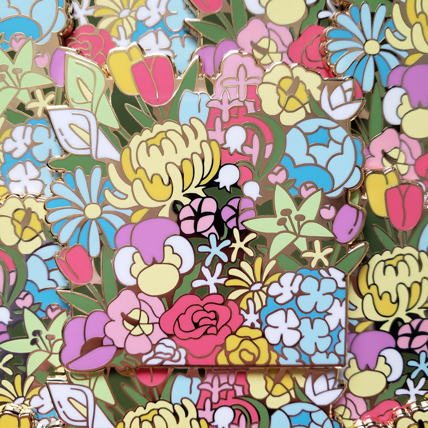 Closeup of the gold cast pin which features a dense garden of many different flowers. The flowers are an assortment of different colors to represent the rainbow pride flag.