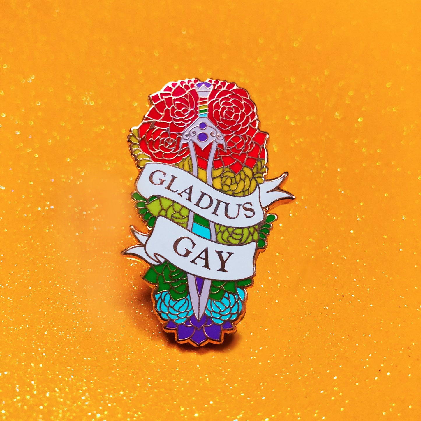 The goldcast pin features a gladius sword in a bed of flowers in rainbow pride colors. A ribbon trails across the front and reads "Gladius Gay"