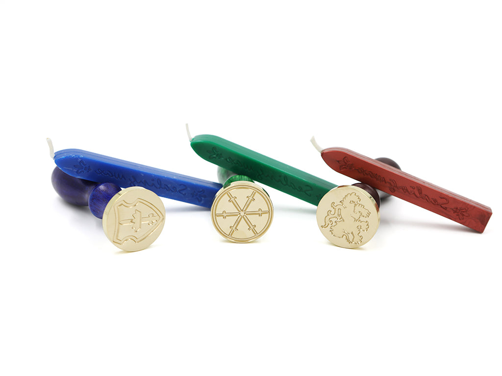 Three wax seals laid on their sides to reveal the seal in gold with their corresponding sealing waxes leaning across each seal. From left to right: Tortall shield seal, George's swords seal, and Alanna's lioness seal.