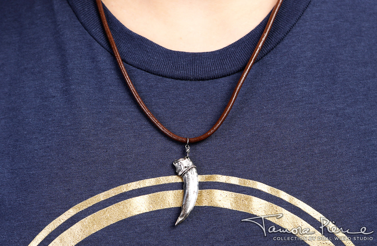 Model wearing silver badger claw pendant on brown necklace cord against a dark blue shirt.