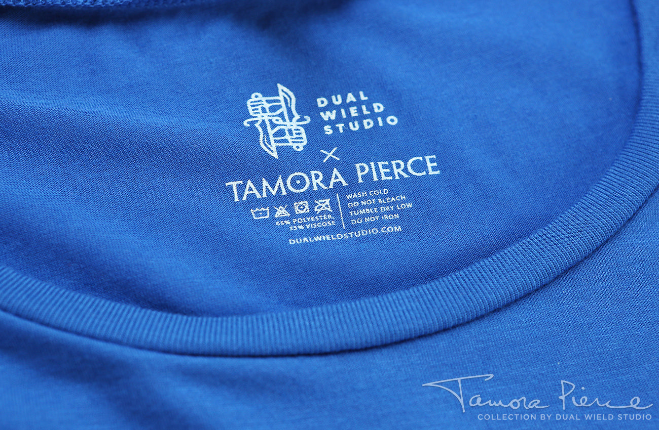 Closeup of printed-on Dual Wield Studio x Tamora Pierce tag with garment care below.