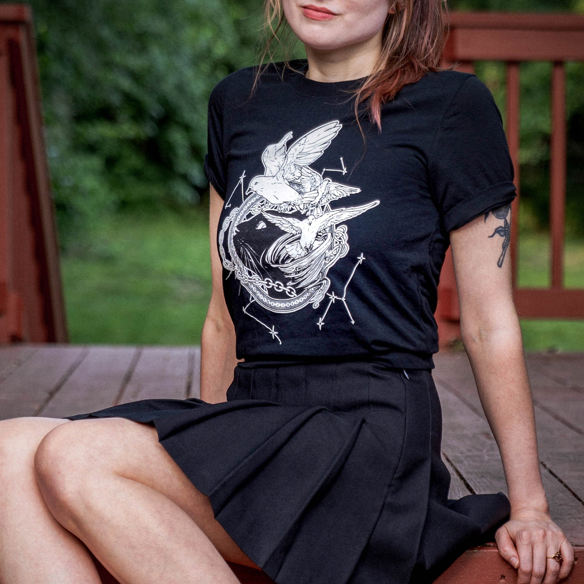 A model wearing the Faithful and the Dust Spinners black tee paired with a matching black pleated skirt.