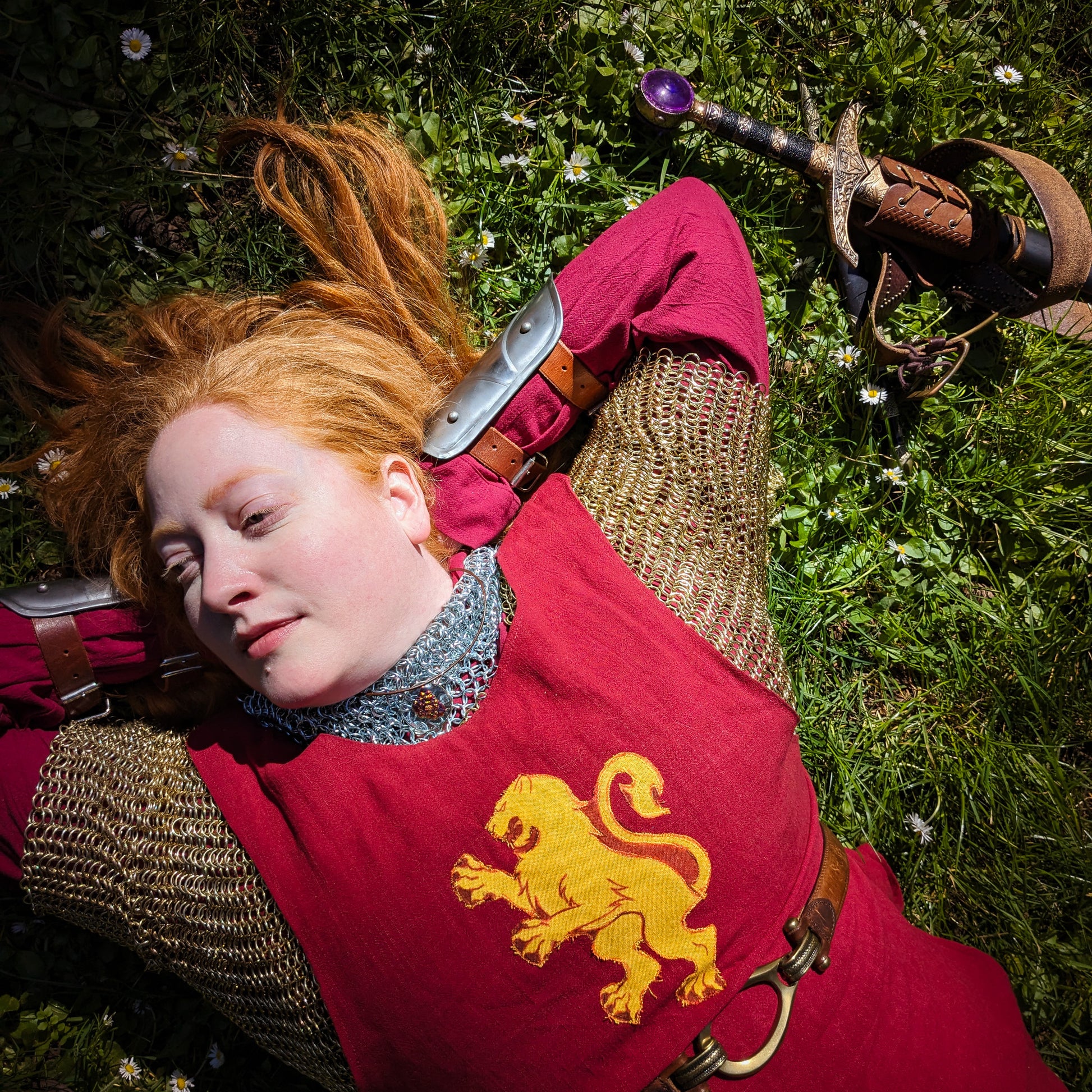 a model wearing chainmail and a red and gold Lioness Rampant tabard wears the ember glass pendant.