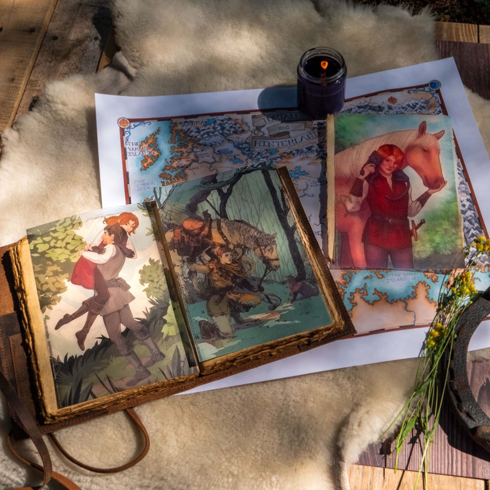 Two page overlays are placed within an aged brown leatherbound journal. The third page overlay is placed beside it, on top of the Tortall map and surrounded by cozy cabin props.