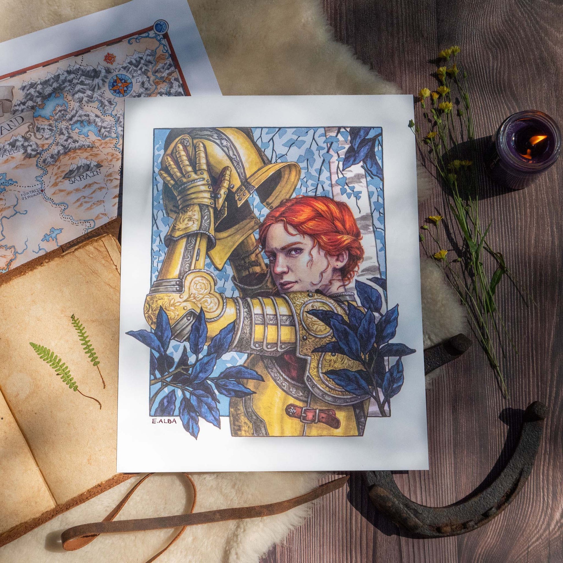 The Alanna the Lioness Limited Edition Print surrounded by a candle, flowers, a horseshoe, and other cozy props.