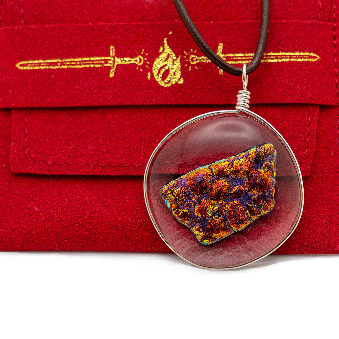 the ember glass pendant on top of the red jewelry pouch. The red pouch is visible through the clear parts of the pendant and the pouch has a gold bow and arrow design on the back.