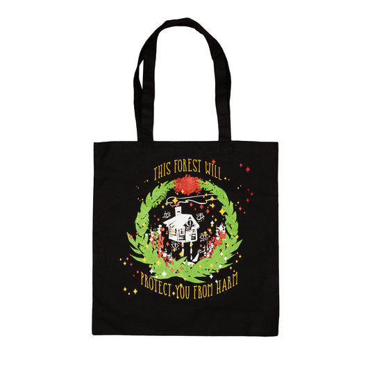 A flat lay photo of a black tote that has a white sketchy outline of baba yaga’s house surrounded by open white eyes. A green wreath with gold and red diamond-shaped sparkles is printed around the house. The arced top text reads “This forest will,” and the bottom text reads “protect you from harm.” 