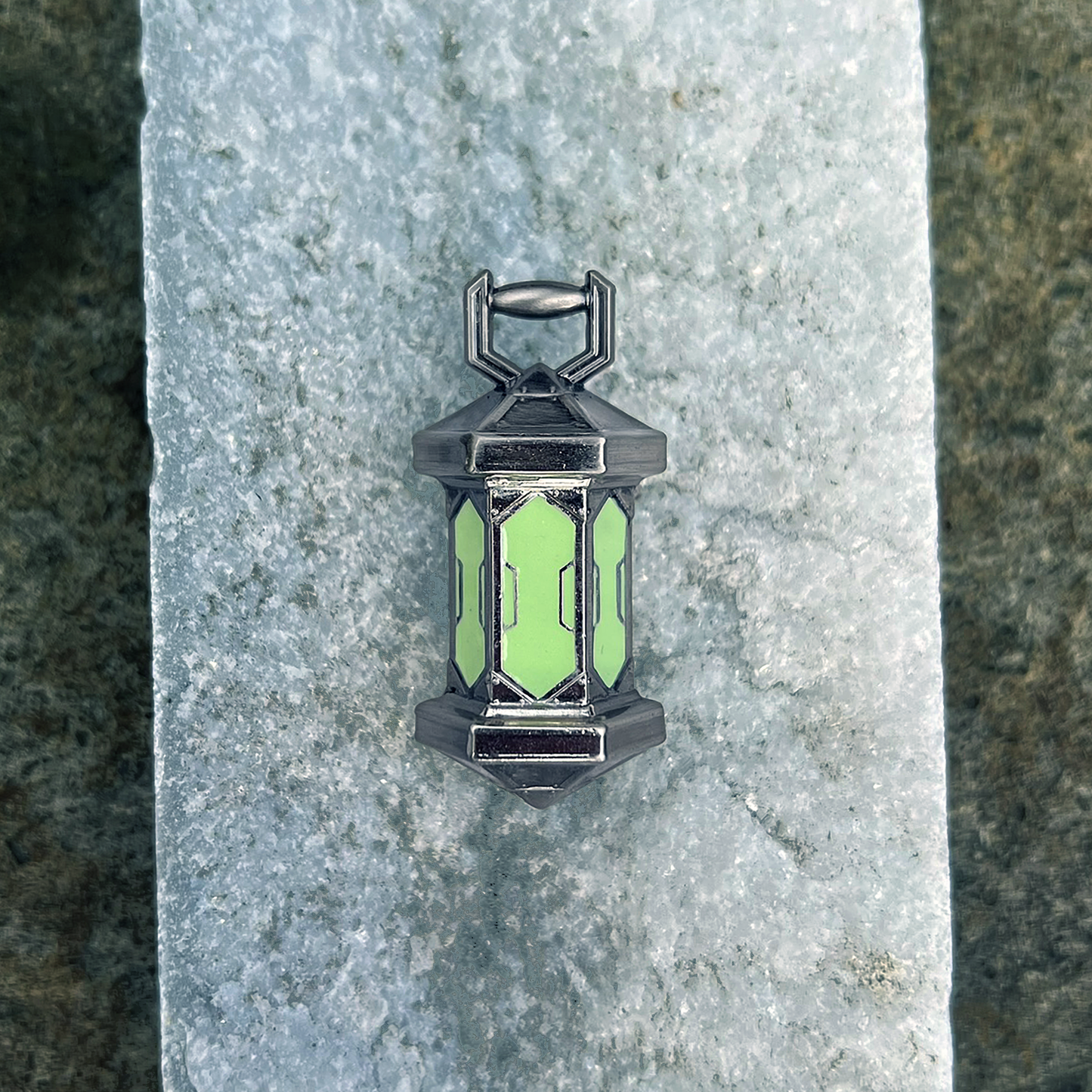 A photo from above of the Gloaming Lantern Pin lying on a granite stone.