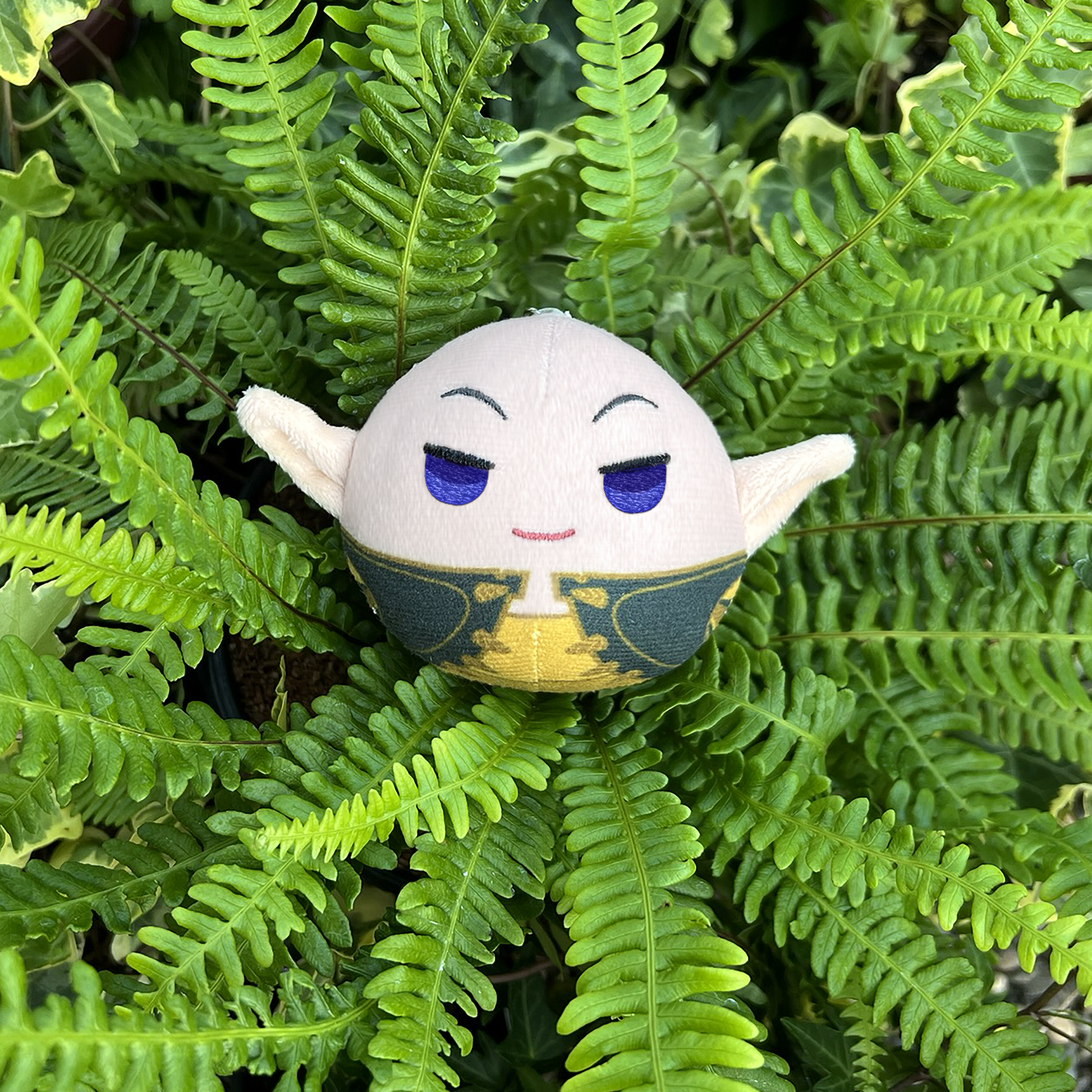 A photo from above of the Solas Keychain Plush resting in a thick bundle of green ferns.