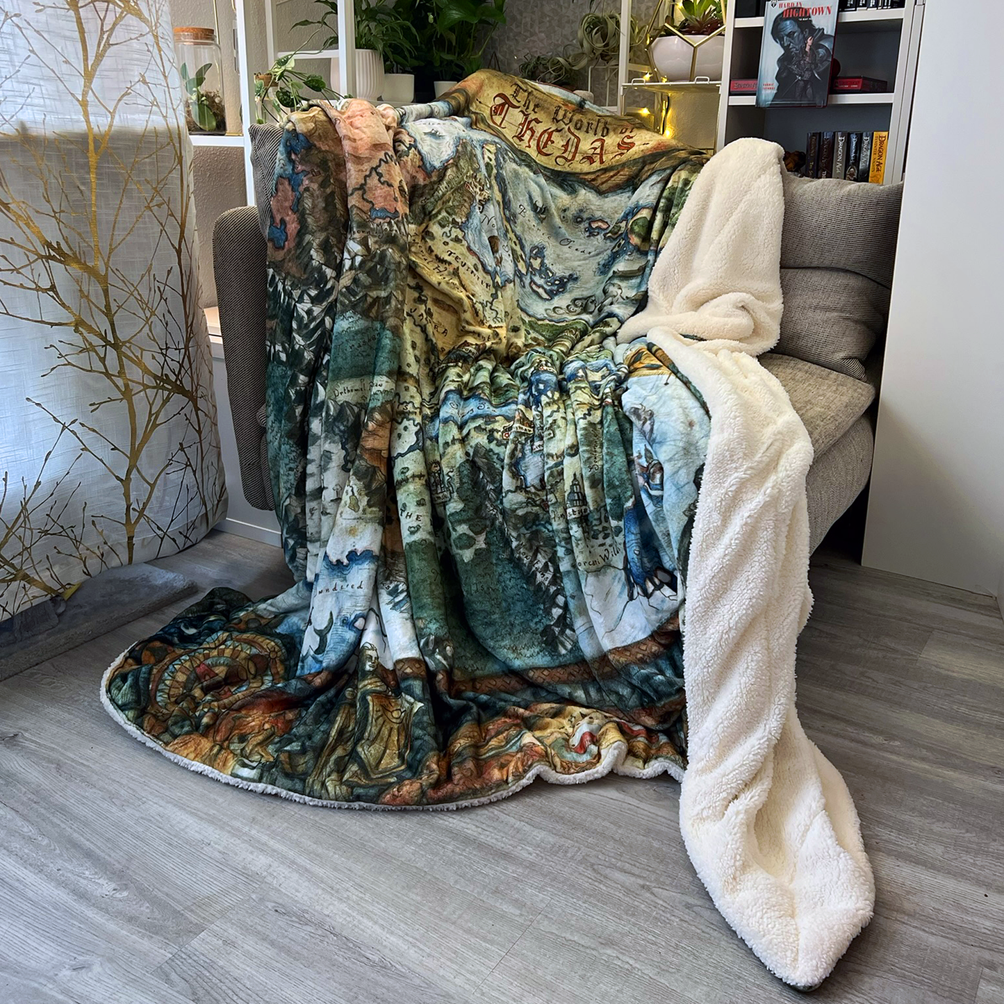 The plush Thedas Map Blanket is draped casually over a corner sofa, showing its sherpa lining.