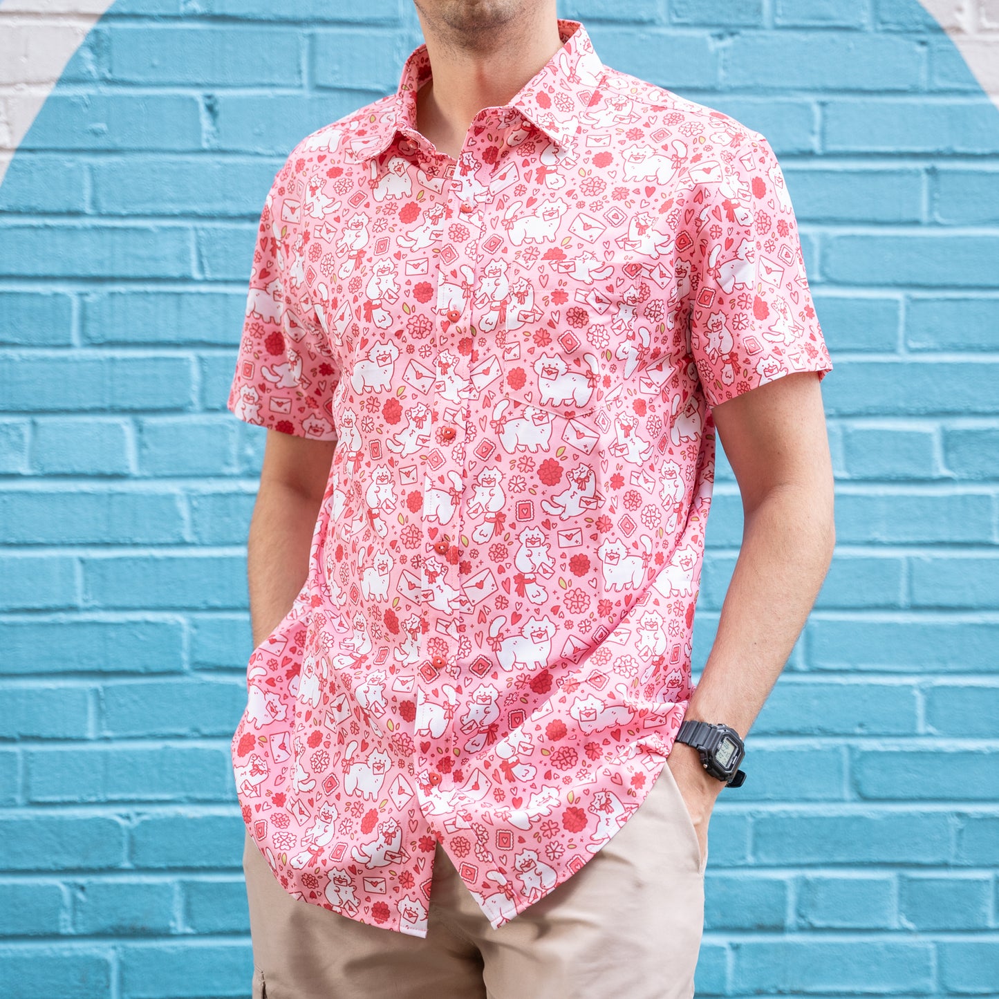 A model casually stands wearing the pink Love Leter Button Up in front of a painted wall that makes the bright and light pinks pop.