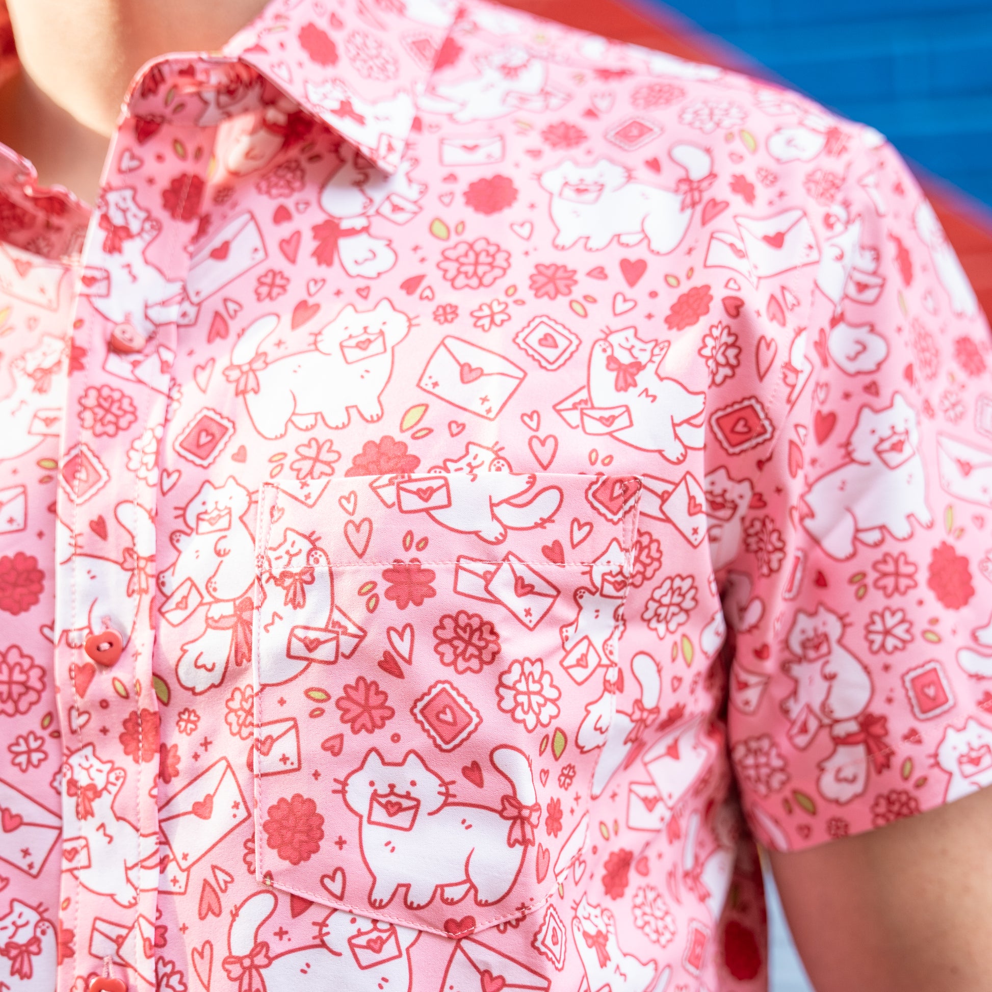 A closeup of the left breast pocket of the Love Letter Button Up, showing little heart-stamped letters and white cats interacting with them.