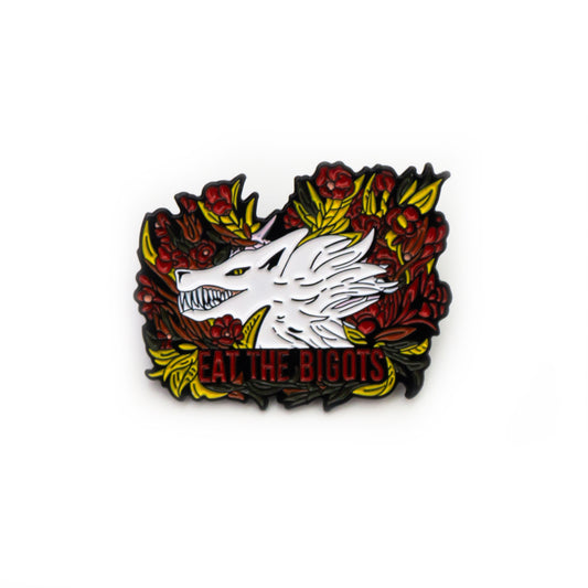 A product photo of an enamel pin with a white wolf savagely grinning on a bed of red roses with yellow leaves. Text below the wolf reads “EAT THE BIGOTS.”