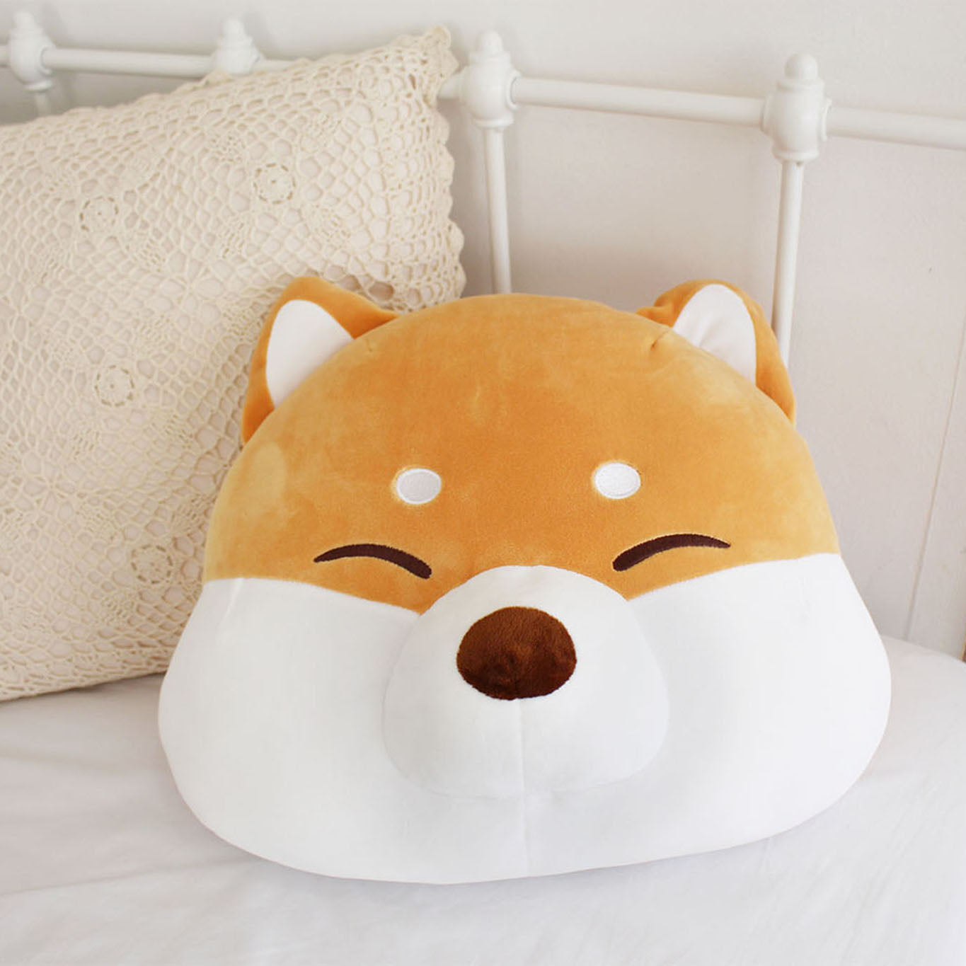 Shiba face cushion sits on a white iron frame bed with square white crochet pillow.