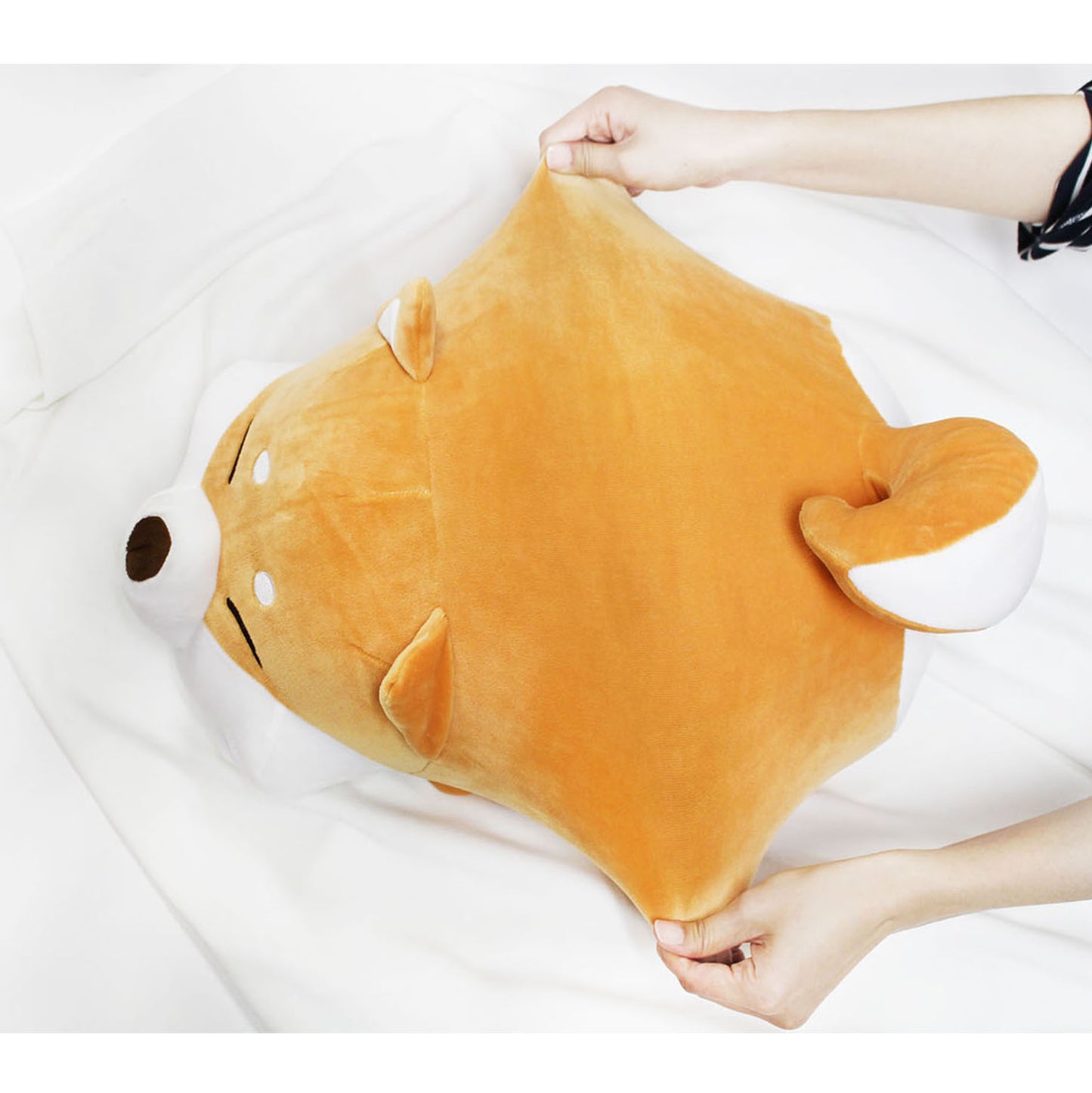 Top view of model stretching the Shiba cushion's middle on a white blanket.