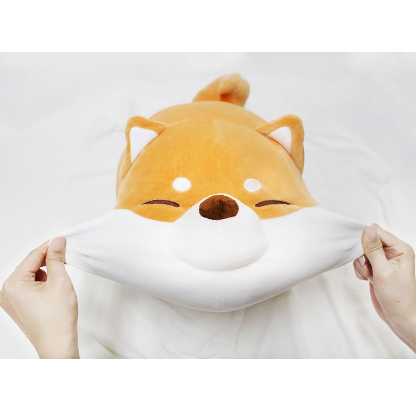 Front view of model stretching Shiba cushion's cheeks on a white blanket.