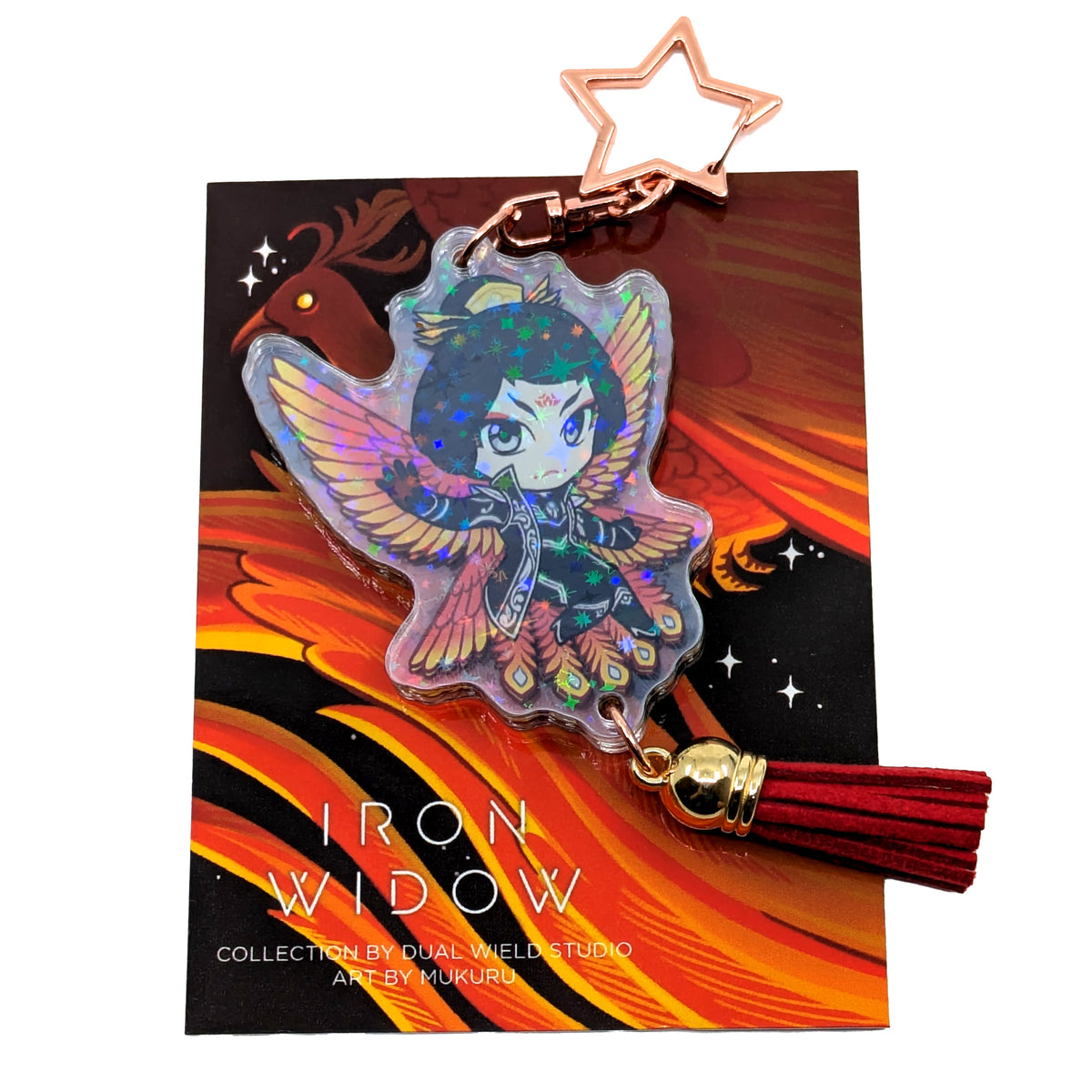 A product photo of Side 1 of the Zetian Holographic Charm. Zetian is illustrated with black and white jacketed outfit and fiery-colored bird wings behind them. The charm has a star shaped clasp, a red tassel, and the acrylic has a holographic effect. The charm is attached to its backing card, which has an illustration of a red feathery phoenix with a glowing yellow eye.