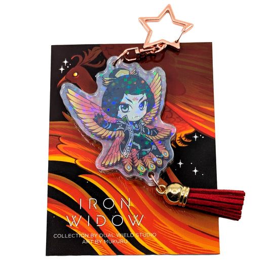 A product photo of Side 1 of the Zetian Holographic Charm. Zetian is illustrated with black and white jacketed outfit and fiery-colored bird wings behind them. The charm has a star shaped clasp, a red tassel, and the acrylic has a holographic effect. The charm is attached to its backing card, which has an illustration of a red feathery phoenix with a glowing yellow eye.