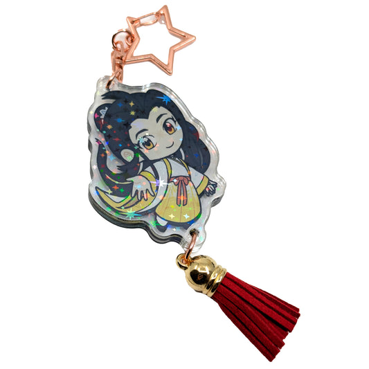 A product photo of Side 2 of the Yizhi Holographic Charm. Yizhi is illustrated in white and yellow traditional clothing and is extending a hand toward the viewer. The charm has a star shaped clasp, a red tassel, and the acrylic has a holographic effect.