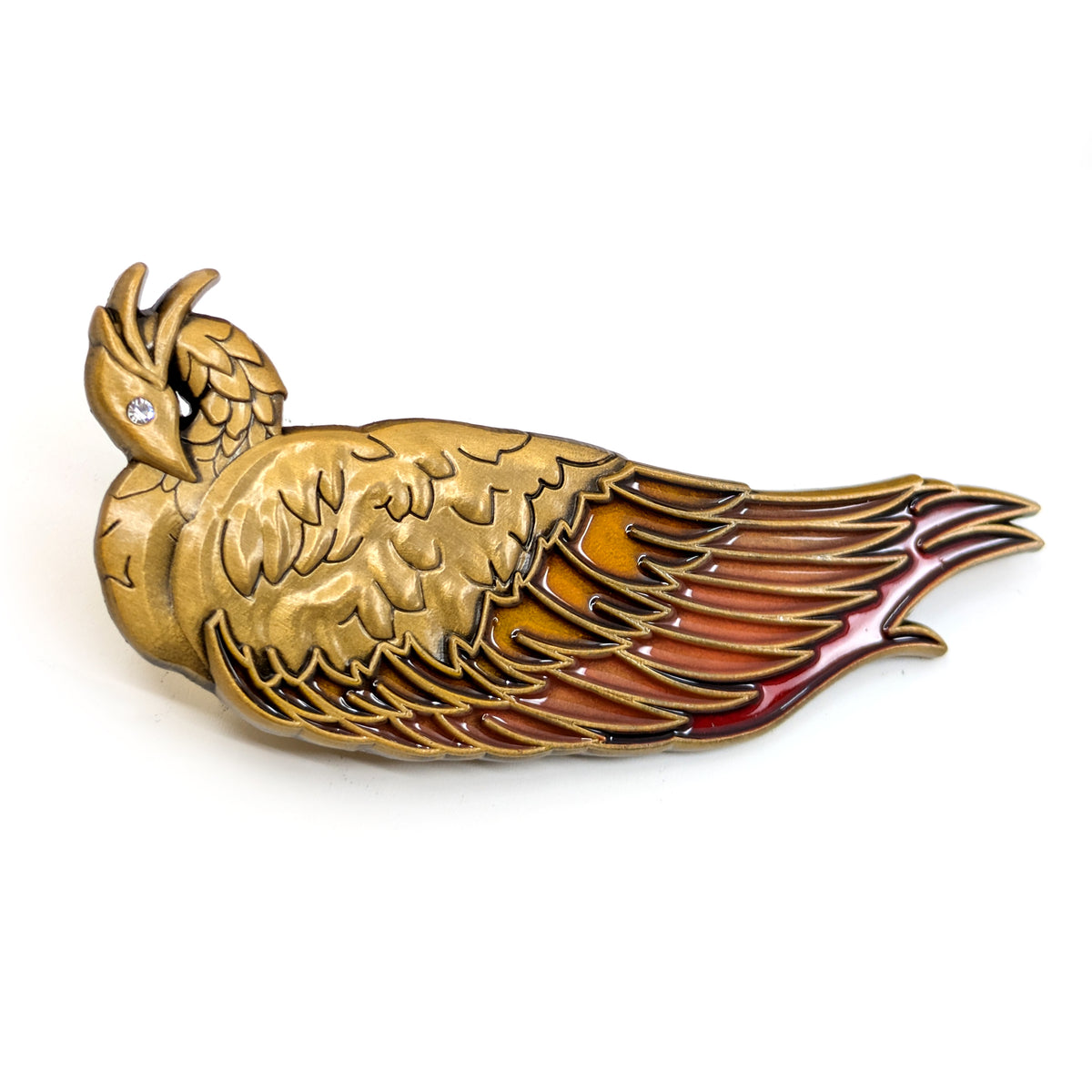 A product photo of a golden cast phoenix hair clip with orange and red enamel primary feathers. The phoenix is resting, wings closed, with its head curled inward toward its swan-like neck.
