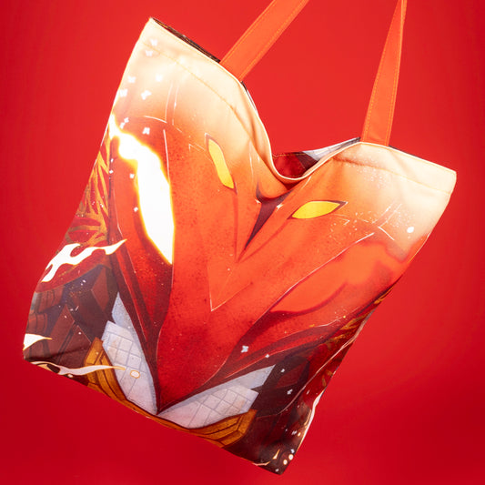 A product photo of the opposite side of the Iron Triangle Tote Bag on a red background. This side has an illustration of the Vermillion Bird’s face gritting its mecha teeth. One eye flames in white and the other in red.