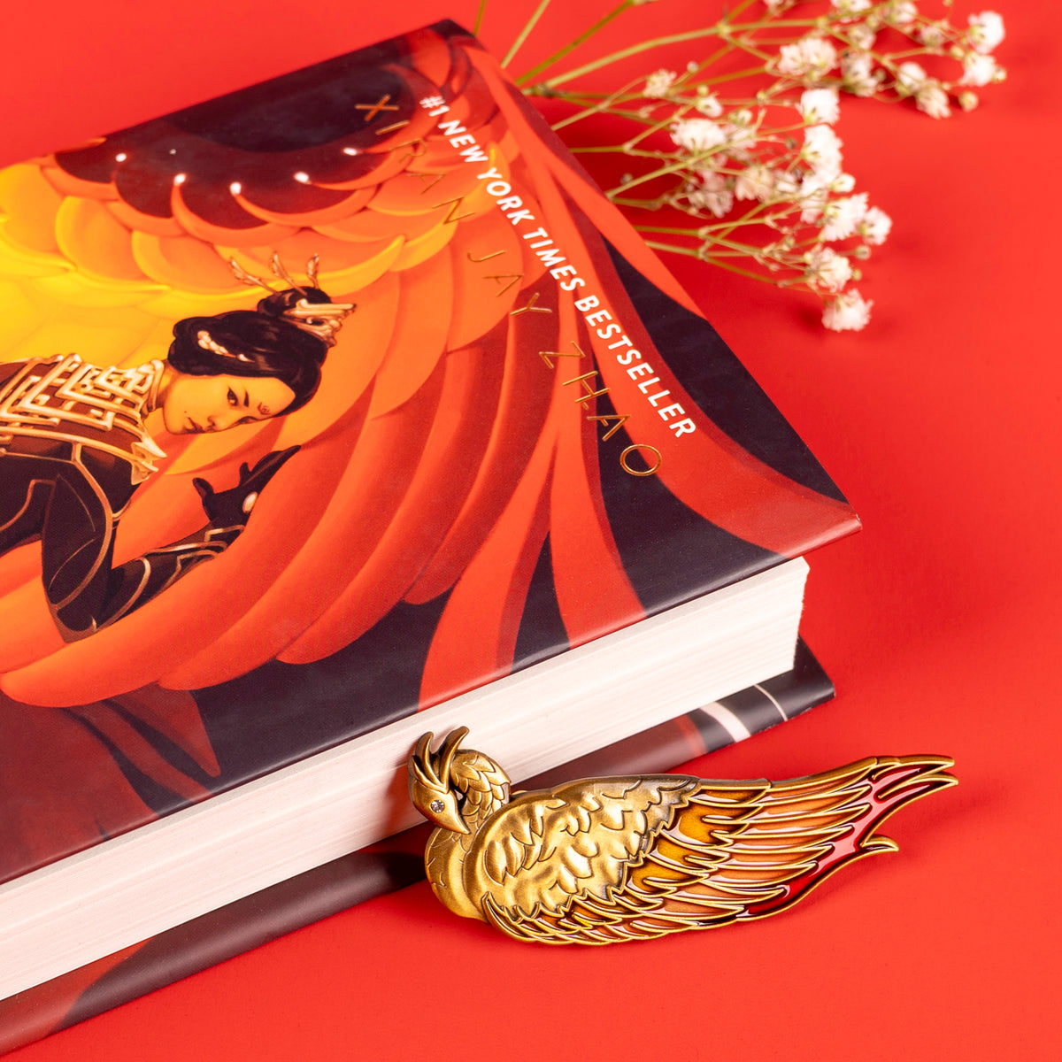 The golden Vermillion Bird hair clip is resting on a red background along the fore edge of an Iron Widow hardcover copy.