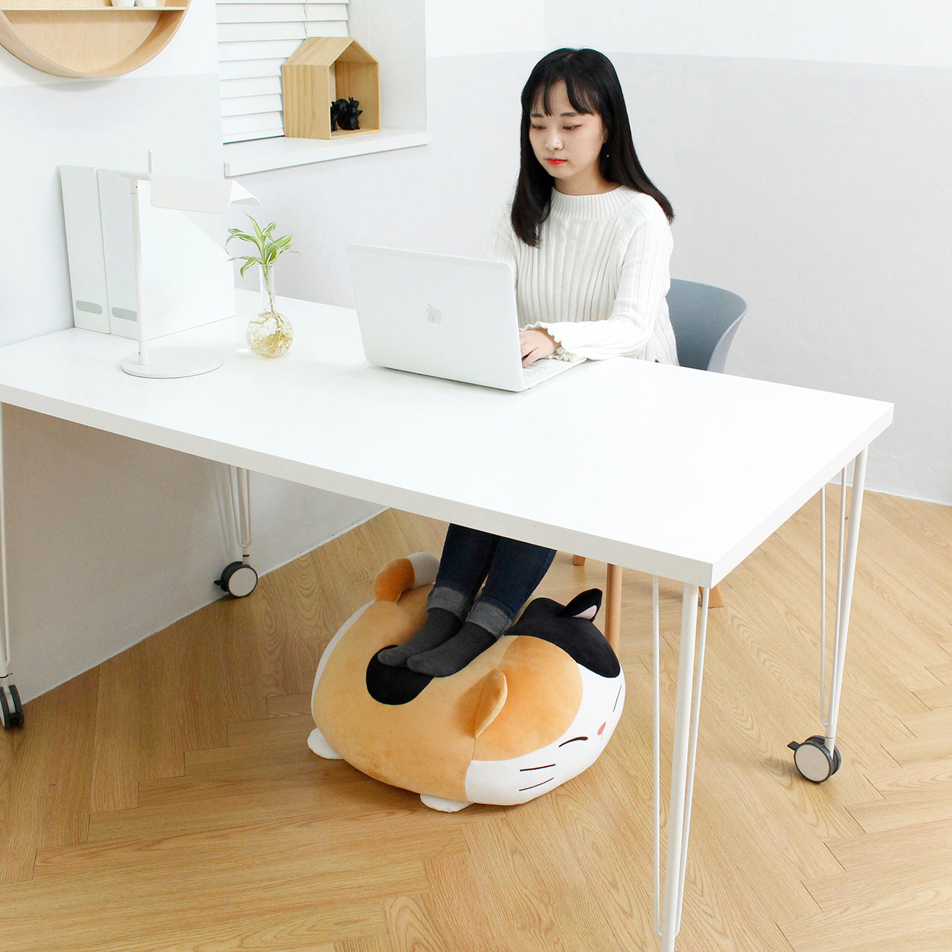 Model sits at desk using their laptop with their feet propped up on Camang pillow.