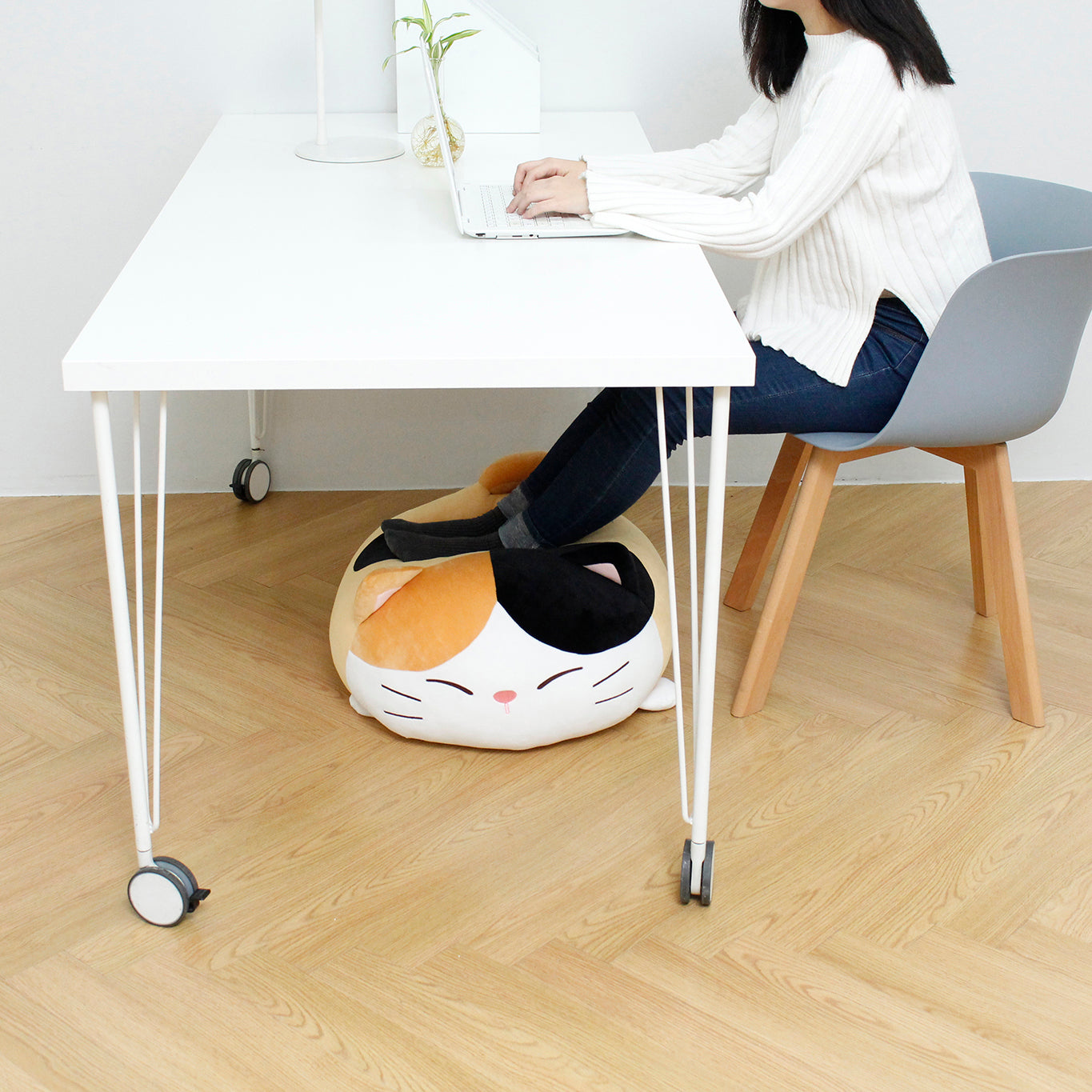 Side view of model sitting at desk using their laptop with their feet propped up on Camang pillow.