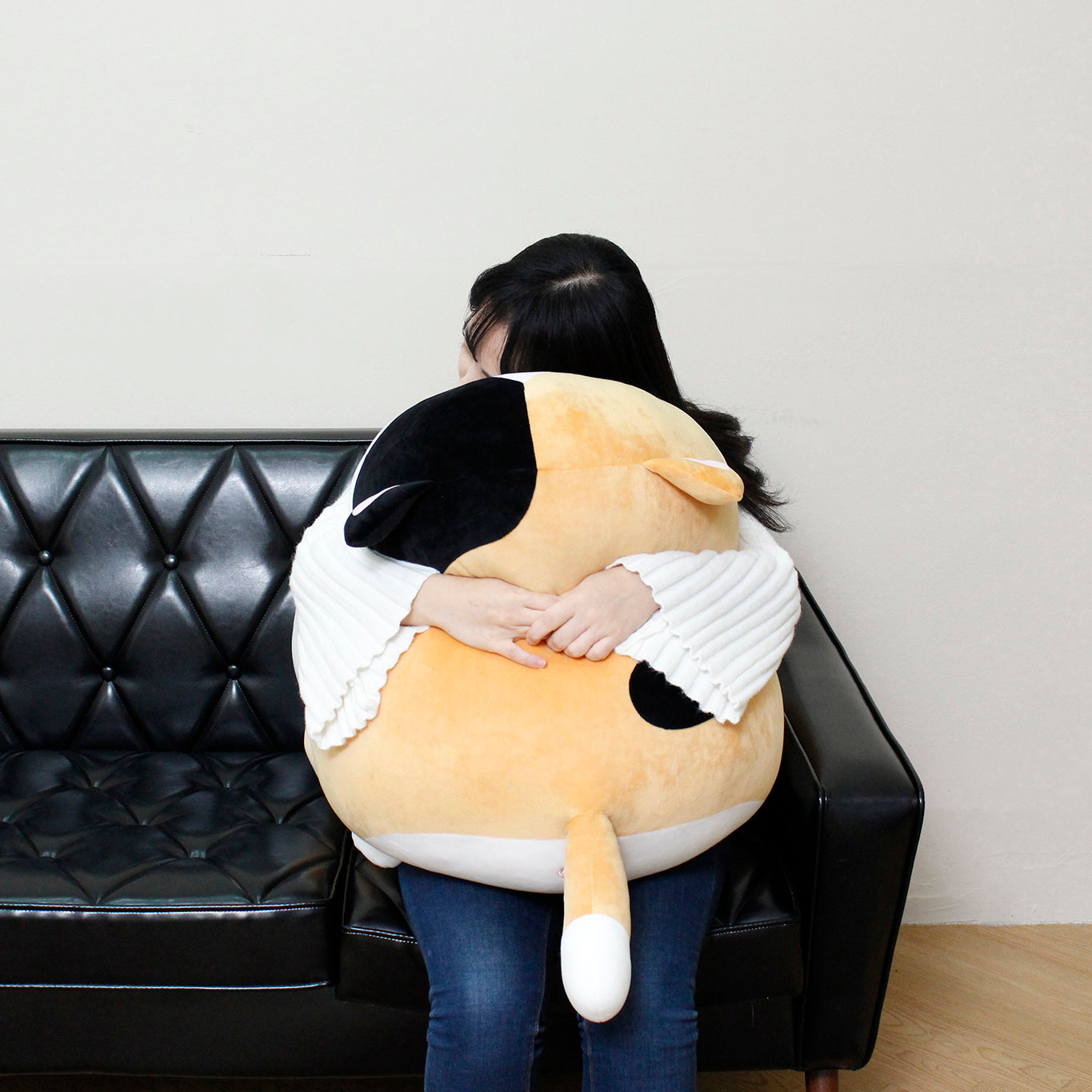 Model sits on black, leather couch giving Camang pillow a big hug.