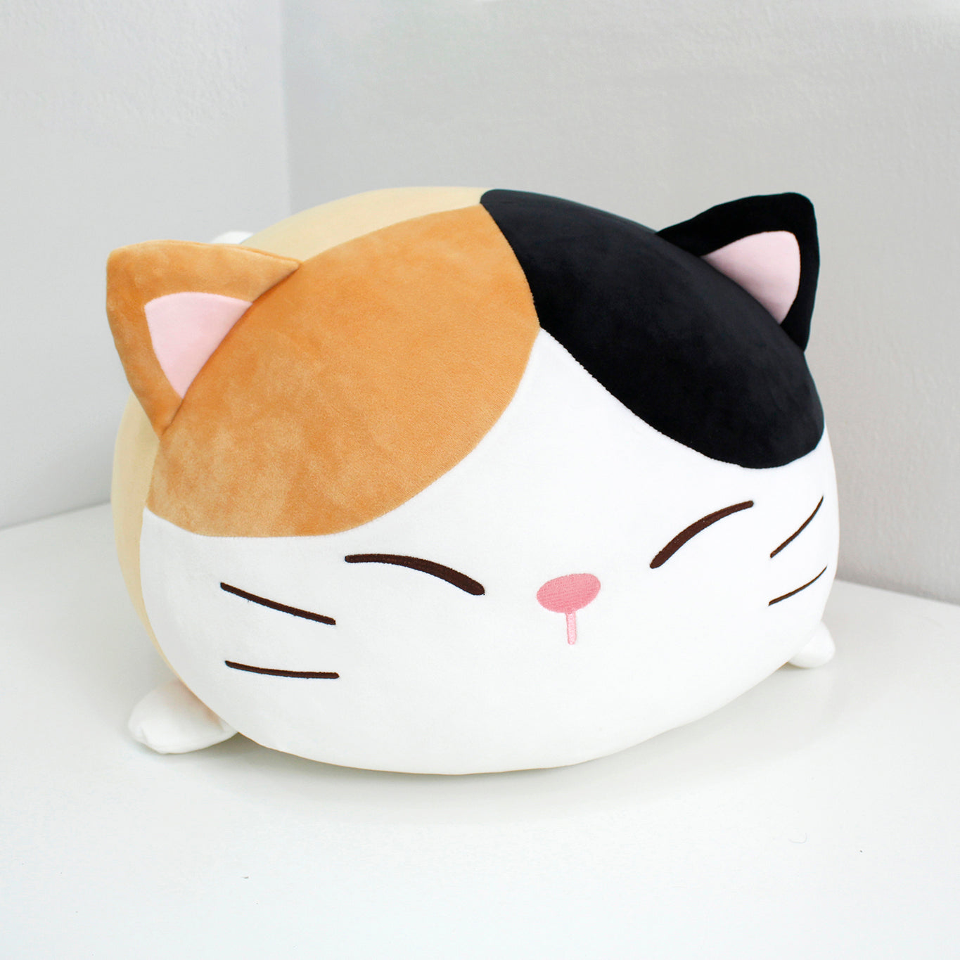 Front view of calico cat Camang pillow. Its embroidered eyes are closed.