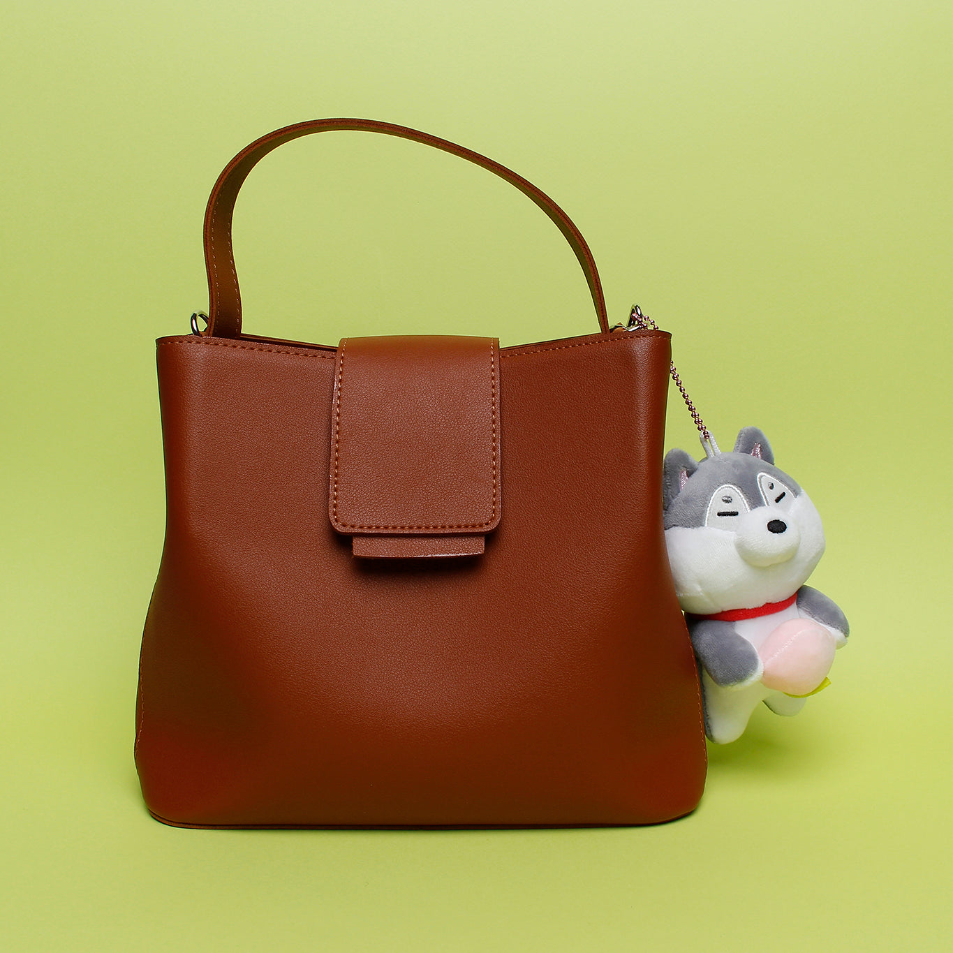 Grey shiba with peach keyring plush attached to brown purse on lime green background.