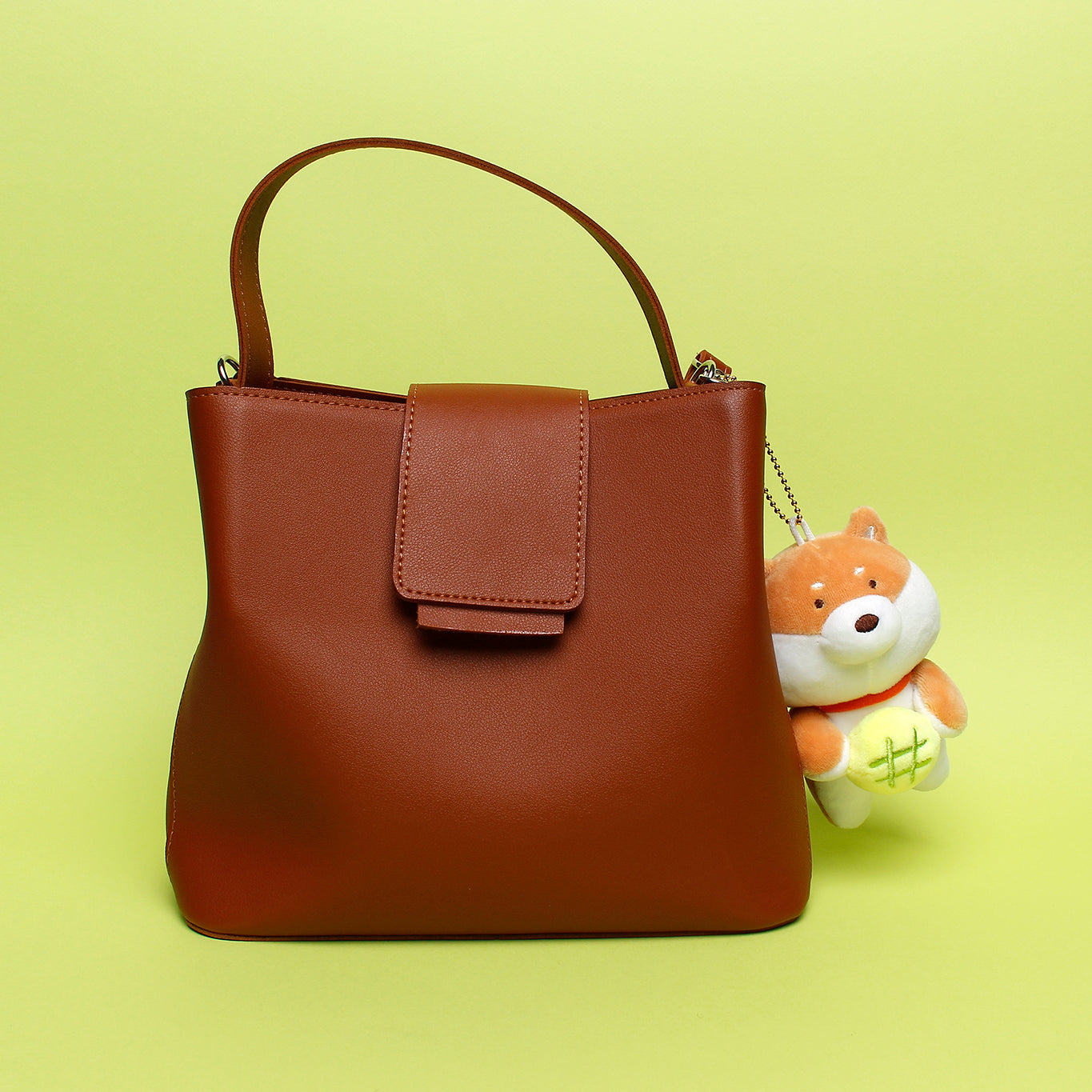 Tan shiba with green roll keyring plush attached to brown purse on lime green background.