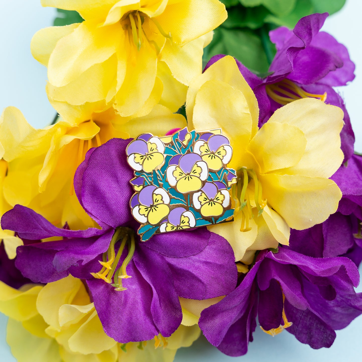 A lifestyle photo of the Non-Binary Pansies Pin resting atop a bundle of flowers matching the pin's purple and yellow colors.