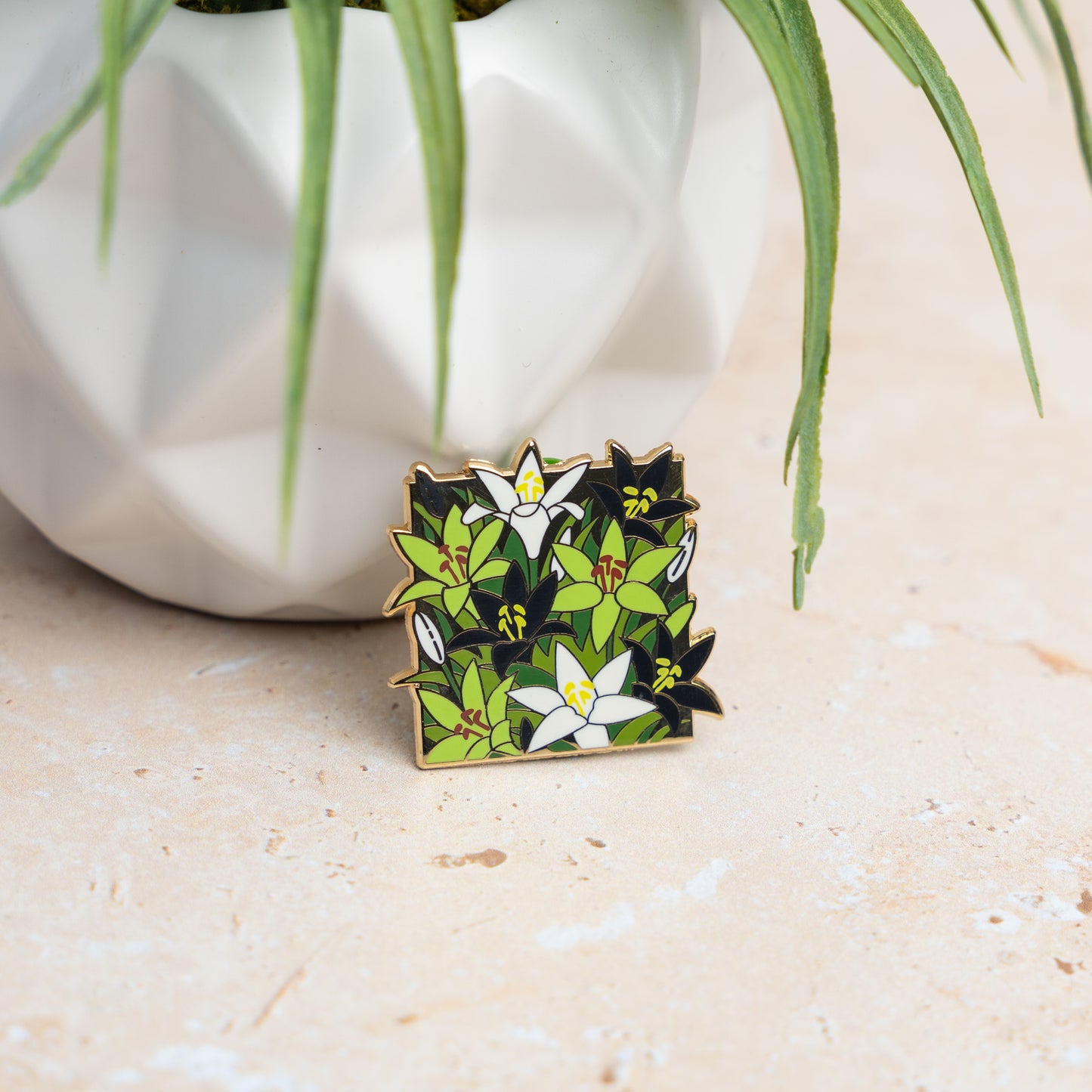 A lifestyle photo of the Aro Lilies pin leaning on a white planter.