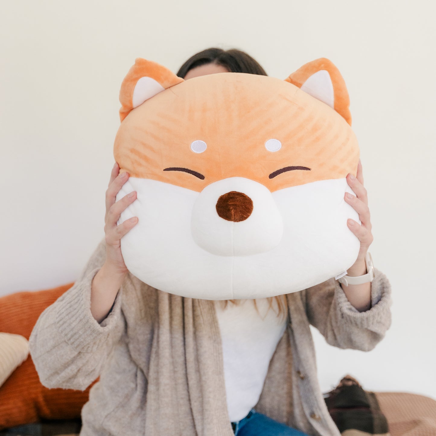 Model in a sweater holding the Shiba face cushion in front of her own.