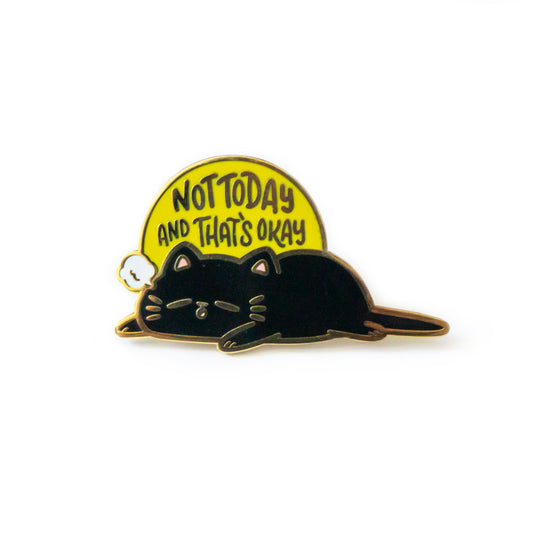 A product photo of an enamel pin depicting a black cat laying flat on its tum with its legs splayed. A small white cloud poof is coming from its mouth. A yellow sun rises behind it and says “Not Today and That’s Okay.