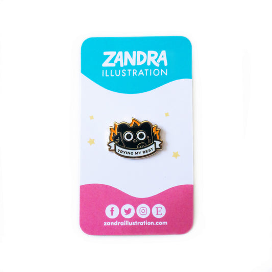 A product photo of the Trying My Best black cat Pin on its cyan, white, and magenta wavy colorblocked backing card. The backing card says Zandra Illustration at the top in white, and displays icons that signify the artist is on facebook, twitter, instagram, and etsy along the bottom of the card